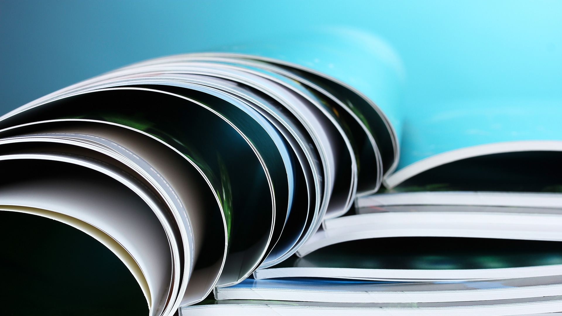 Close up showing curved pages of many open booklets, stacked together.