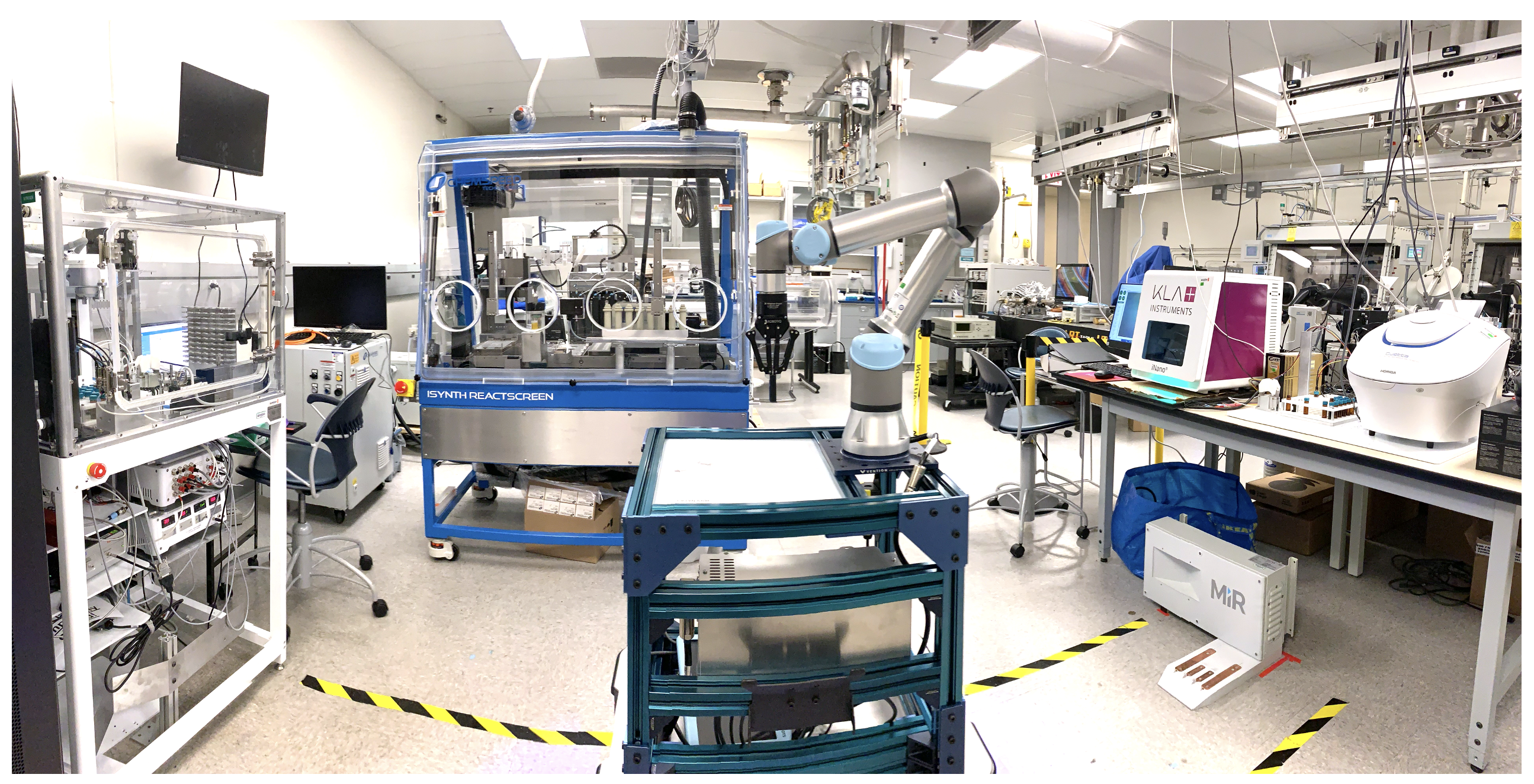 interior of laboratory room with multiple large pieces of equipment, monitors, and smaller pieces of equipment on tables; there are two yellow and black striped tape strips on floor